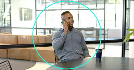 Talking man wearing button-down shirt holding smartphone to ear at office lounge with coffee cup....