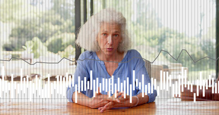 Speaking senior woman wearing blue blouse sitting at wooden table at home, showing waveform overlay....