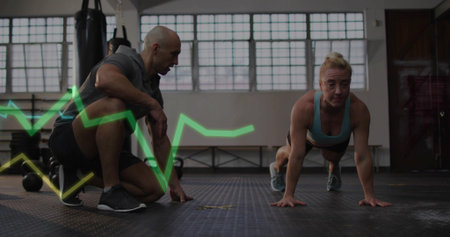 Performing plank trainee wearing blue bra, shorts on rubber floor, weights, ECG line, copy space....