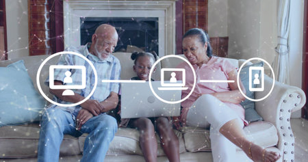 Smiling grandparents and granddaughter leaning over laptop on sofa at home, with connectivity icons....