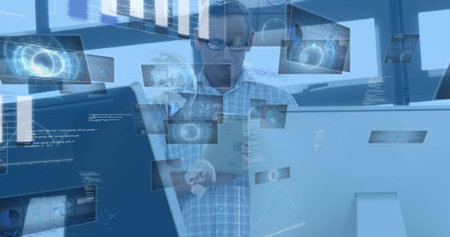 Studying man with glasses, checked shirt, holding tablet at desk with holographic panels. Technology, office, visualization, analytics, interface, workspace, futuristicの写真素材