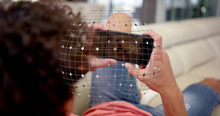 Reclining man wearing coral tee and jeans holding smartphone on living room sofa, showing AR grid....