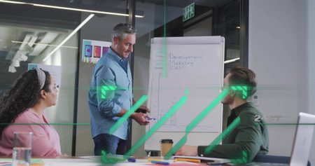 Presenting man in light-blue shirt writing on flip chart in glass conference room, with laptop....