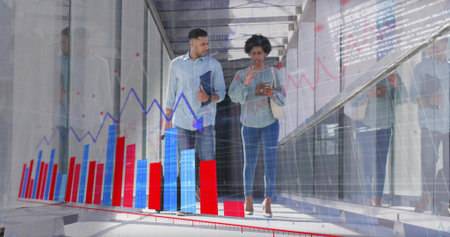 Walking business-casual colleagues reviewing tablet and folder in glass corridor, showing charts....