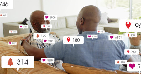 Sitting father and son in plaid denim shirts, leaning on tan sofa at home, showing notifications....