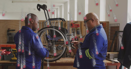 Two technicians in blue coveralls repairing manual wheelchair rear wheel on workbench with phone....