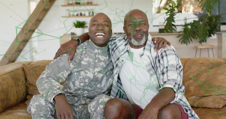 Laughing soldier hugging dad on brown sofa in living room, wearing camo uniform and plaid shirt....