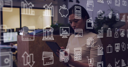 Holding tablet, woman wearing top checking data in office near glass partition with finance icons....