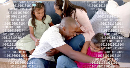 Playing family laughing on gray sofa, dad reaching toward girl in pink dress. Parents, kids, couch,...