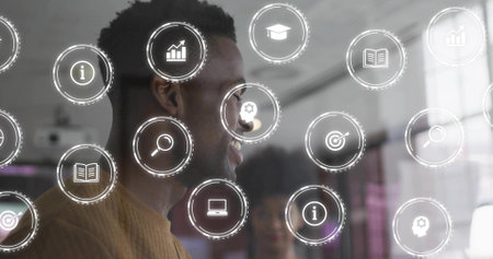 Smiling man in brown sweater standing by glass in office, showing translucent UI icons, copy space....