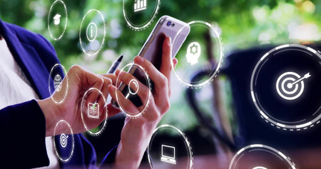 Holding smartphone mid-adult woman tapping screen at cafe wearing dark blazer with pen and AR icons....