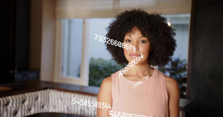 Standing woman facing camera in dining nook in sleeveless pink top, banquette and numeric overlays. Portrait, interior, natural, light, window, plants, digitsの写真素材