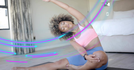 Stretching woman wearing pink sports-bra, blue high-waist shorts on home mat, showing wrist tracker....