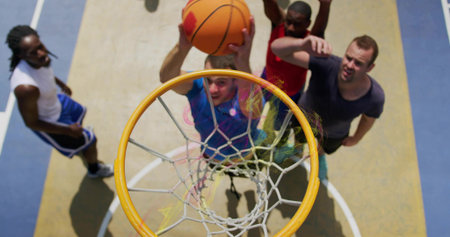 Jumping male in blue shirt reaching for dunk under rim at outdoor court, with orange basketball....