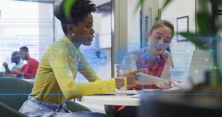 Pointing, two women in yellow, coral working in office at round white table with laptop overlay....