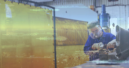 Grinding man in blue PPE operating grinder at bench with clamp, sparks, yellow curtain, copy space....