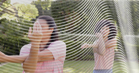 Standing woman in pink top covering face, extending arm in yard with wavy panel, copy space....