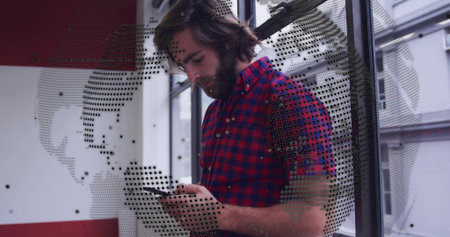 Checking bearded man wearing red-blue checkered shirt, using phone in lobby with dotted globe decal....