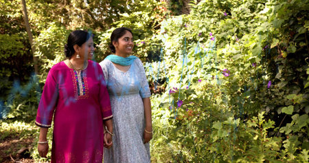 Walking mother and daughter holding hands along garden path, wearing kurta and dupatta, copy space....