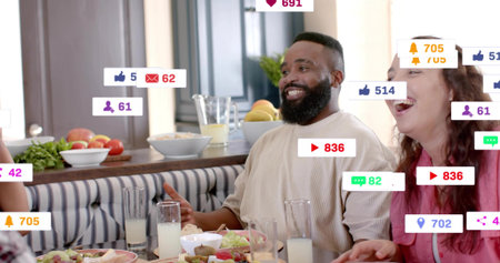 Laughing man in cream top and woman in pink chatting at dining table, with plates, notifications....