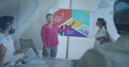 Presenting woman in bright pink blouse pointing at wall screen showing infographic in meeting room....