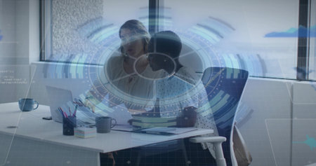 Reviewing two women in business-casual leaning over laptop and papers at office, HUD overlay....