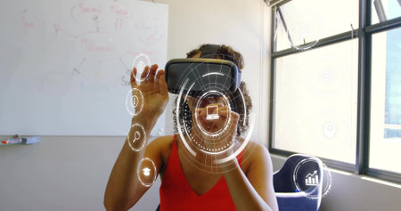 Manipulating AR icons like laptop and chart, female in red top with VR headset in office. Goggles,...