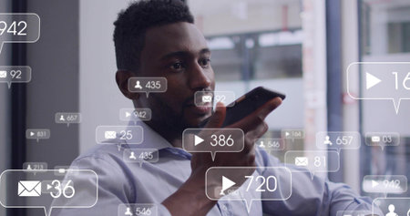 Speaking adult man wearing light blue shirt holding smartphone near mouth at office, social bubbles....