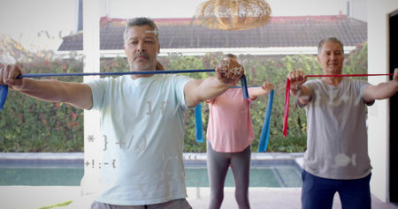 Holding blue band, center man wearing light blue tee, gray shorts stretching on patio by pool....