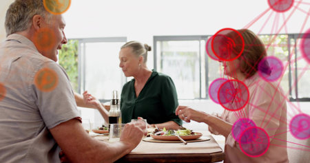 Sitting three adults in casual wear sharing salads at wooden dining table with glass bottle overlay....