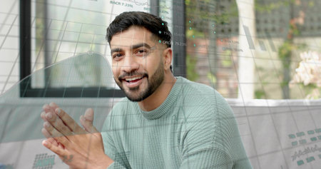 Smiling man in light green sweater sitting on sofa by glass window, overlaid data charts. Presenter,...