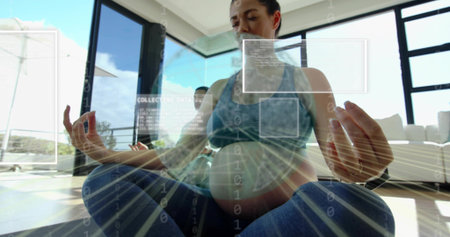 Sitting pregnant woman meditating on yoga mat in bright living room wearing sportswear. Pregnancy,...