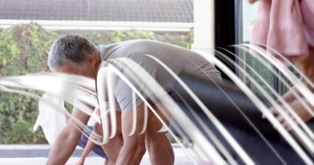 Bending mature man crawling on knees poolside, wearing gray shirt and dark shorts with arcing jets....