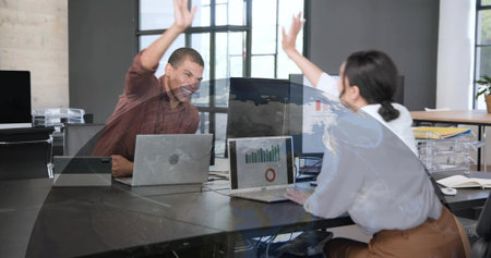 High-fiving colleagues in maroon shirt, white blouse in office, plexiglass, laptops with charts....