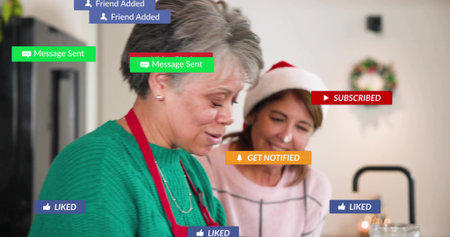 Making cookies senior woman red apron at kitchen counter while companion in Santa hat. Baking, cozy,...