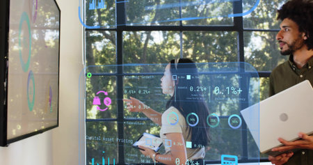 Reviewing, two professionals wearing shirts viewing on-glass dashboards with tablet by grid window....