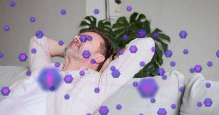 Reclining man wearing pale shirt hands behind head looking upward on sofa with plant purple overlay....