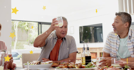 Raising glass, man in light-gray shirt over orange tee at dining table, plates and star overlays....