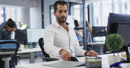 Reaching bearded man in white shirt touching smartphone on desk with monitor in office. Colleagues,...