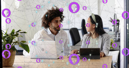 Discussing colleagues in office in business casual using laptop, tablet with plant and purple nodes....