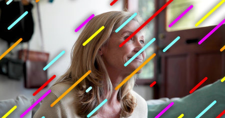 Smiling mature woman wearing light knit sweater sitting on sofa, multicolored streaks overlaying....