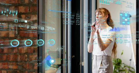 Analyzing woman studying data charts on glass partition in office in white blouse, copy space....