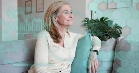 Sitting woman wearing cream cardigan at home, resting on teal pillow and showing smartwatch HUD....