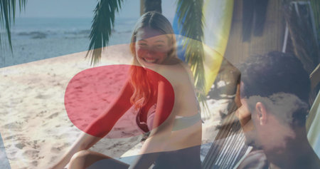 Smiling woman sitting in bikini on sandy beach, man reclining in hammock under cabana color overlay....