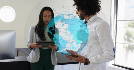 Reviewing colleagues in white shirt and gray blazer scanning tablets in office, holographic globe....