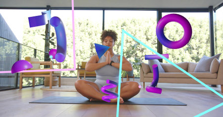 Meditating woman in gray activewear sitting on yoga mat at home, wearing tracker with AR graphics....