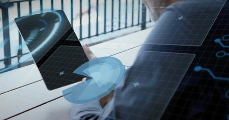 Holding tablet, man in blazer tapping screen at balcony slatted table, showing AR graphics, railing....
