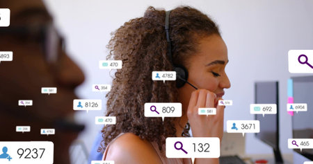 Adjusting woman in light top speaking into black headset in call center, showing monitors and icons....