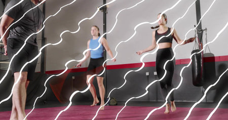 Jumping three adults in athletic wear, barefoot, using jump ropes at fitness studio, heavy bag. Gym, dynamic, motion, group, workout, coaching, enduranceの写真素材