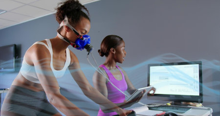 Pedaling female in athletic wear wearing blue metabolic mask with tubing on ergometer in lab....